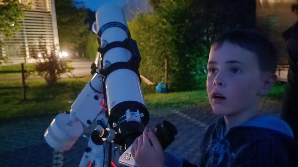 ein junger Mann staunt neben dem Teleskop über den faszinierenden Nachthimmel