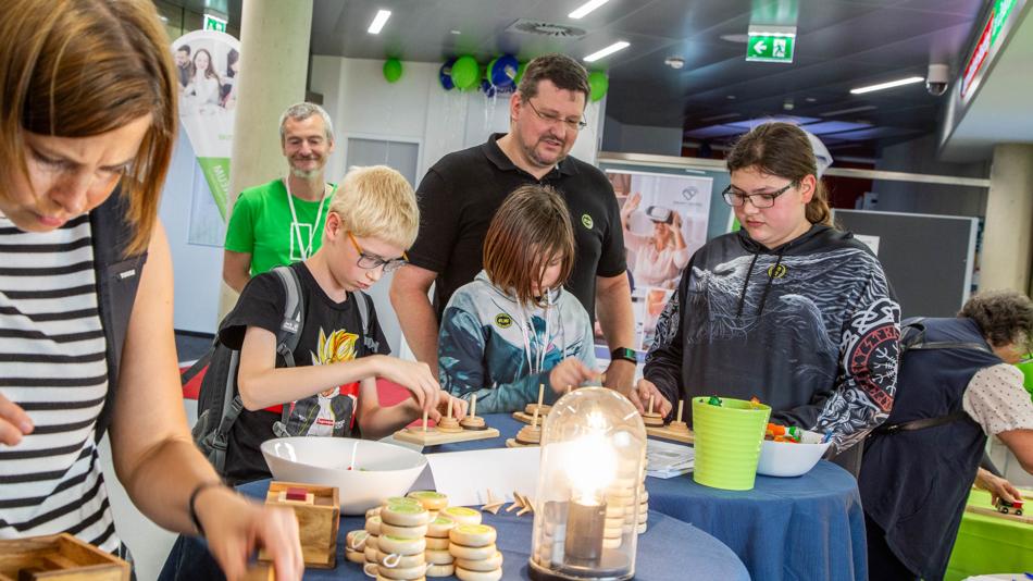 Das Bild zeigt Besucher:innen der Langen Nacht der Forschung an der FH JOANNEUM beim Lösen des Rätselns „Türme von Hanoi“