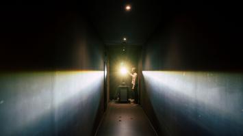 Eine Person in einem schmalen, dunklen Flur bedient ein Messgerät mit einer starken Lichtquelle.
