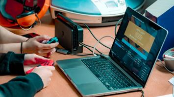 Zwei Paar Hände mit einem Spiele-Controller vor einem Laptop