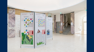 Foyer eines Gebäudes mit Faltwänden, auf denen Affenpuzzle mit Erklärung des Workshops Abenteuer Informatik zu sehen sind
