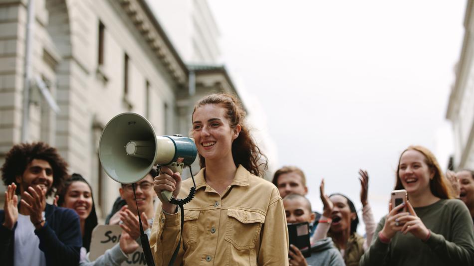 Frau mit Megaphon vor einer Gruppe von Menschen auf der Straße