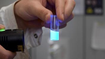 Fluorisizierende Flüssigkeit in einem kleinen Glasgefäß, von einer Hand gehalten.