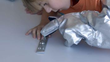 Kind mit Astronautenhandschuh arbeitet mit Schrauben
