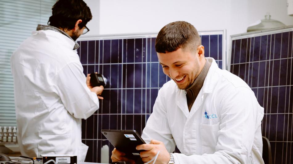 In this laboratory setting, two researchers are conducting near-infrared (NIR) measurements on a photovoltaic (PV) module. One researcher is using a tablet to monitor and record data, while the other operates a device to perform precise NIR analysis, high