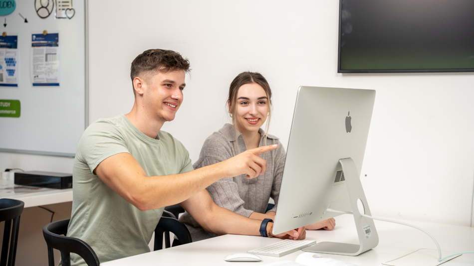 Ein junger Mann und eine junge Frau sehen interessiert in einen Computerbildschirm