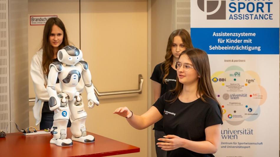 Schülerinnen präsentieren einen humanoiden Roboter, der Sportübungen vorzeigt und ertastbar macht