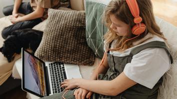 Kind mit Kopfhörern neben Laptop sitzend