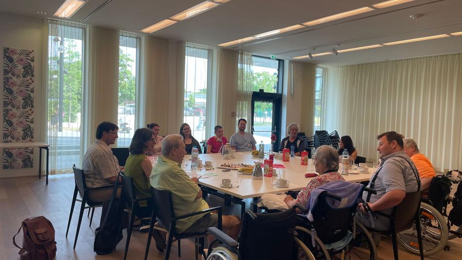 Verschiedene Menschen (Alter, Geschlecht, professionelle Pflegefachkräfte, Schüler:innen, Student:innen, Forschende, Pflegewohnheimbewohner:innen) sitzen um einen Tisch