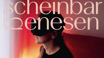 Person in schwarzer Kleidung sitzt seitlich im Bild und trägt eine große schwarze Augenmaske. Über dem Bild liegt der Schriftzug „scheinbar genesen“, Hintergrund in warmen Rot- und Orangetönen.