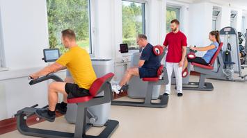 Ein Physiotherapeut betreut 3 Patient:innen an Trainingsgeräten.