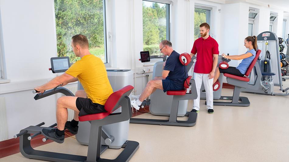 Ein Physiotherapeut betreut 3 Patient:innen an Trainingsgeräten.