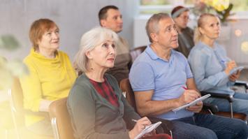 Sechs Personen sitzen in zwei Reihen in einem Raum, schauen nach vorne und machen sich Notizen.