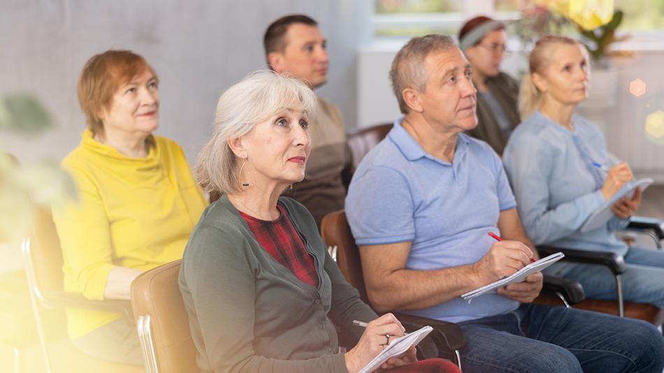 Sechs Personen sitzen in zwei Reihen in einem Raum, schauen nach vorne und machen sich Notizen.
