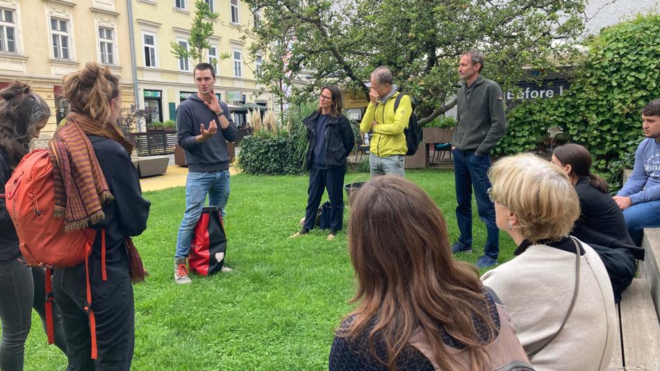 Dieses Bild zeigt eine Station eines Geh-Workshops. Eine Person hält einen Impulsvortrag, weitere Personen hören zu