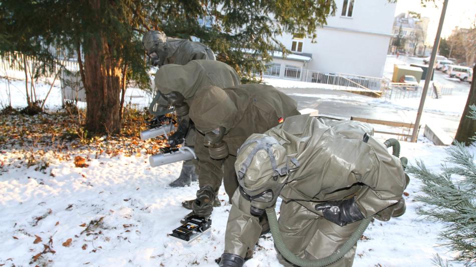 Zwei Personen in Schutzanzügen entnehmen Proben im verschneiten Außenbereich