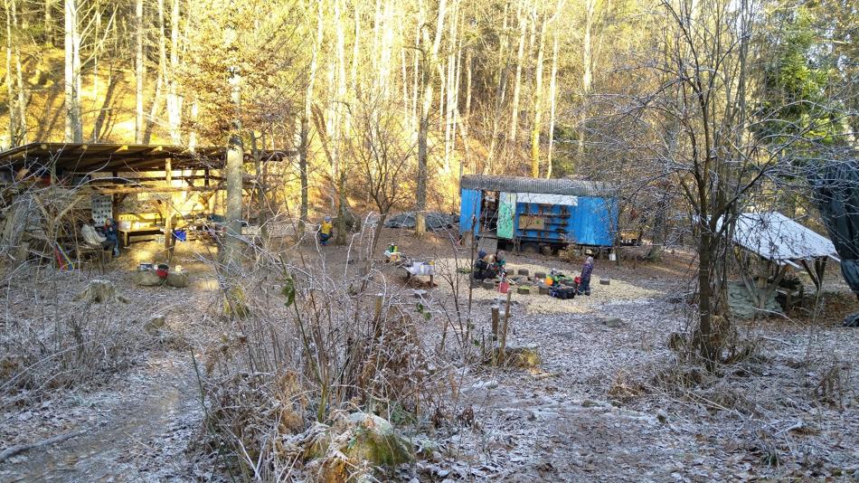 Waldlichtung mit Bauwagen, Unterstand und verstreuten Sitzgelegenheiten im leichten Frost