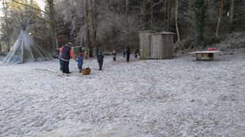 Kinder und Erwachsene auf einer verschneiten Wiese neben Tipi und Holzschuppen
