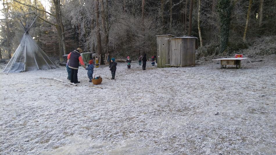 Kinder und Erwachsene auf einer verschneiten Wiese neben Tipi und Holzschuppen