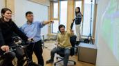 Mehrere Personen testen in einem Labor eine Fahrradsimulation mit Projektion