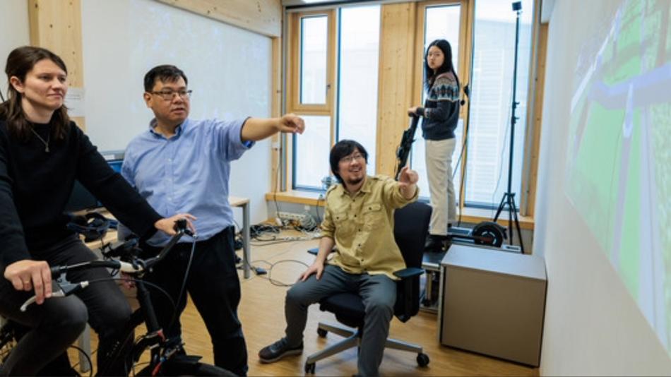 Mehrere Personen testen in einem Labor eine Fahrradsimulation mit Projektion