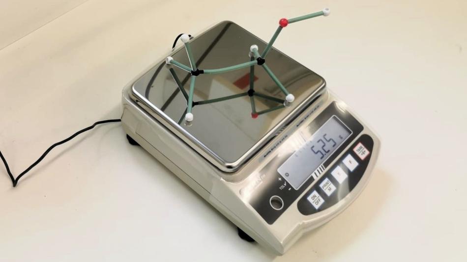 Digitale Feinwaage mit aufgelegtem Molekülmodell auf der Wiegefläche und angezeigtem Messwert im Display