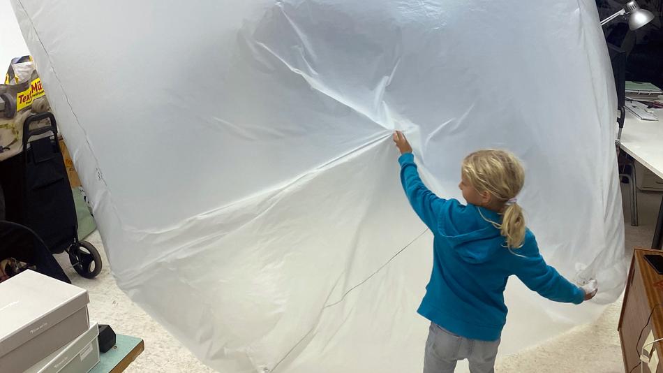 Aufgeblasener, großer Folienwürfel, der von einem Mädchen festgehalten wird.