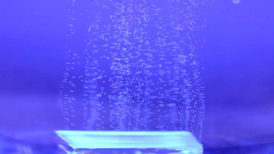 Blauer Hintergrund, unten eine Platte von der kleine weiße Punkte aufsteigen