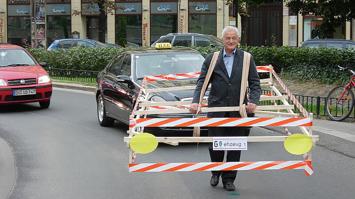 Person mit Holzrahmen in größe eines Autos auf der Straße