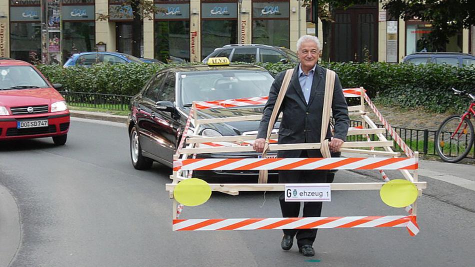 Person mit Holzrahmen in größe eines Autos auf der Straße