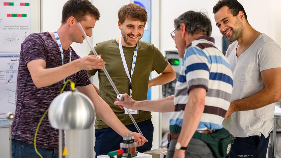 Vier Personen führen ein auf Tisch aufgebautes Experiment durch