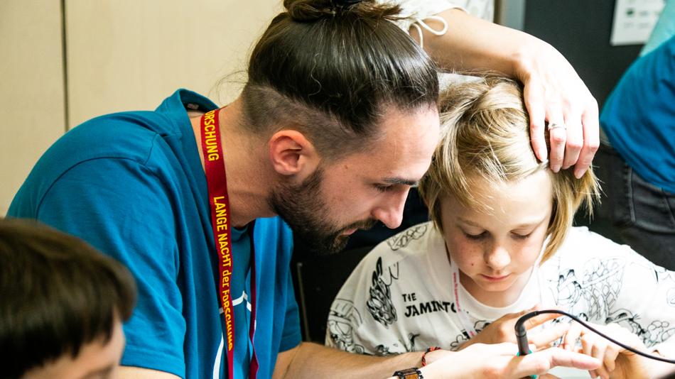 Das Bild zeigt Besucher:innen beim Löten und Basteln bei der Langen Nacht der Forschung