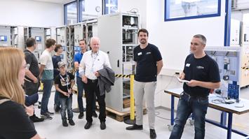 Das Bild zeigt Mitarbeiter:innen von Sprecher Automation und Besucher:innen bei einem Rundgang durch die Fertigung.