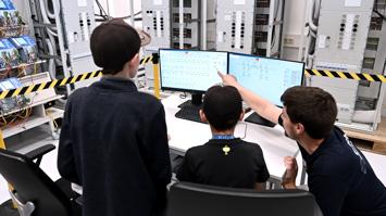 Ein Mitarbeiter von Sprecher Automation erklärt zwei Kindern vor Bildschirmen, wie das Stromnetz funktioniert.
