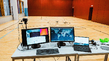 Arbeitsplatz mit Monitoren und Laptop zur Drohnensteuerung in einer Sporthalle