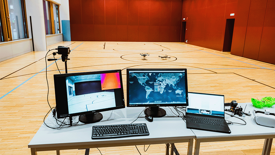 Arbeitsplatz mit Monitoren und Laptop zur Drohnensteuerung in einer Sporthalle