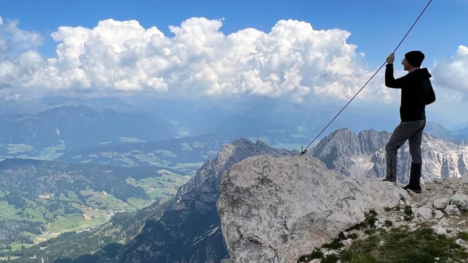 Mann am Gipfel eines Berges mit Blick ins weite Tal