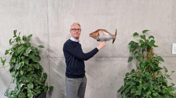 Person steht vor Betonwand und hält einen Fischballon in der Hand