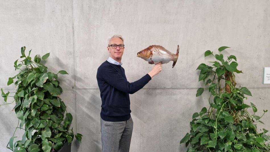 Person steht vor Betonwand und hält einen Fischballon in der Hand