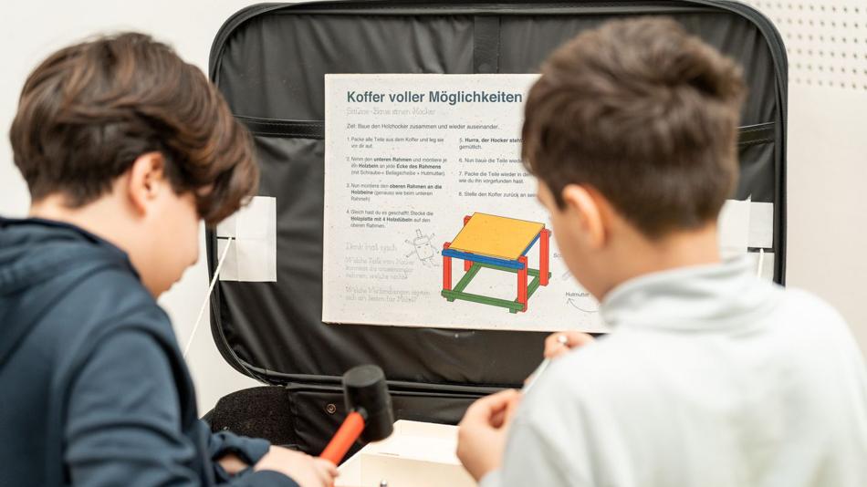 Zwei Burschen von hinten vor einem Koffer