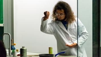 Frau im Laborkittel streut etwas in eine Pfanne