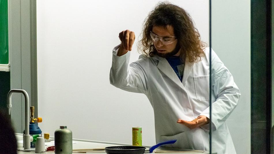 Frau im Laborkittel streut etwas in eine Pfanne