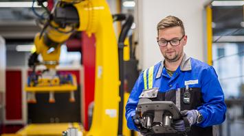 Mitarbeiter bedient ein Steuergerät vor einem großen gelben Industrieroboter