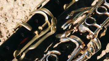 Teile von zwei Klarinetten unterschiedlicher Bauweise, die auf einem Sandboden liegen.