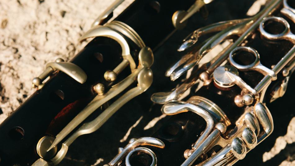 Teile von zwei Klarinetten unterschiedlicher Bauweise, die auf einem Sandboden liegen.