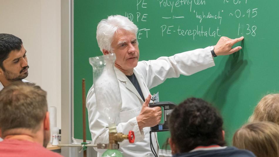 Das Bild zeigt eine Lehrperson an einer Tafel, die etwas erläutert