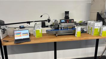 Bildschirm zeigt Spezial-Software-Analyse, daneben Kaffeeverpackungen und eine Siegelstation