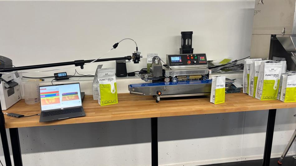 Bildschirm zeigt Spezial-Software-Analyse, daneben Kaffeeverpackungen und eine Siegelstation