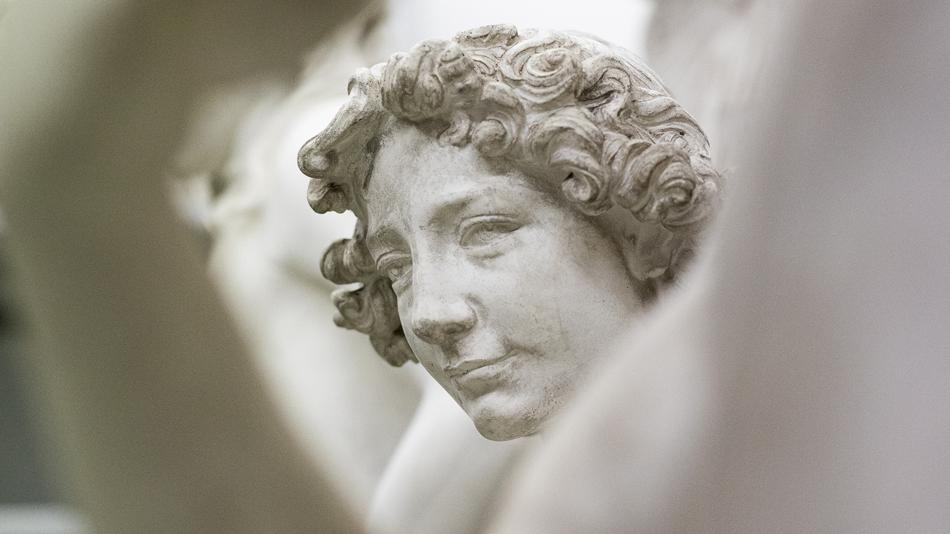 Kopf einer weiblichen Statue aus Gips, blickt zwischen unscharfen Statuen durch