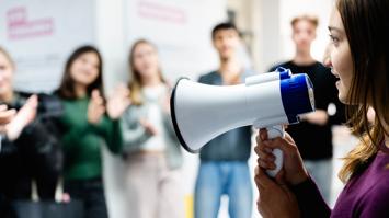 Junge Frau mit Megaphon vor applaudierenden jungen Menschen